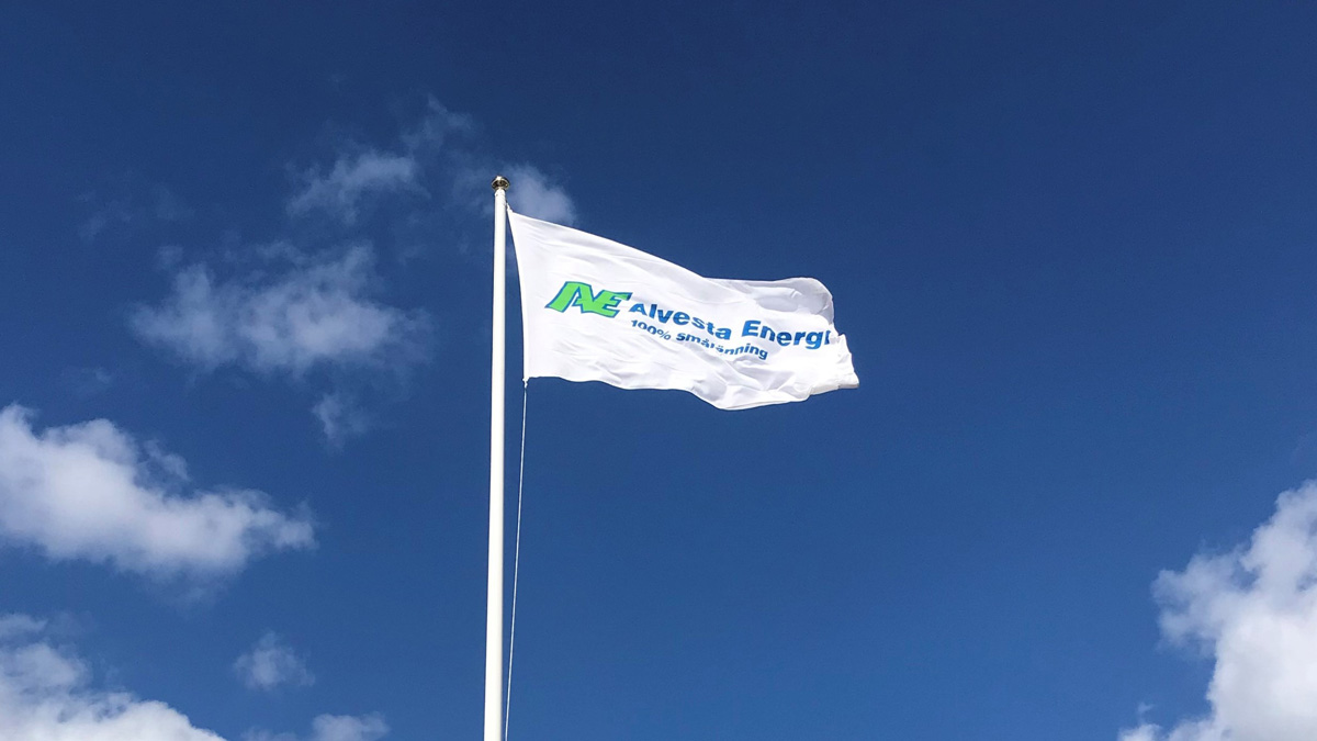 En vit flagga med Alvesta Energis logotyp på vajar mot sin stång mot en blå himmel.